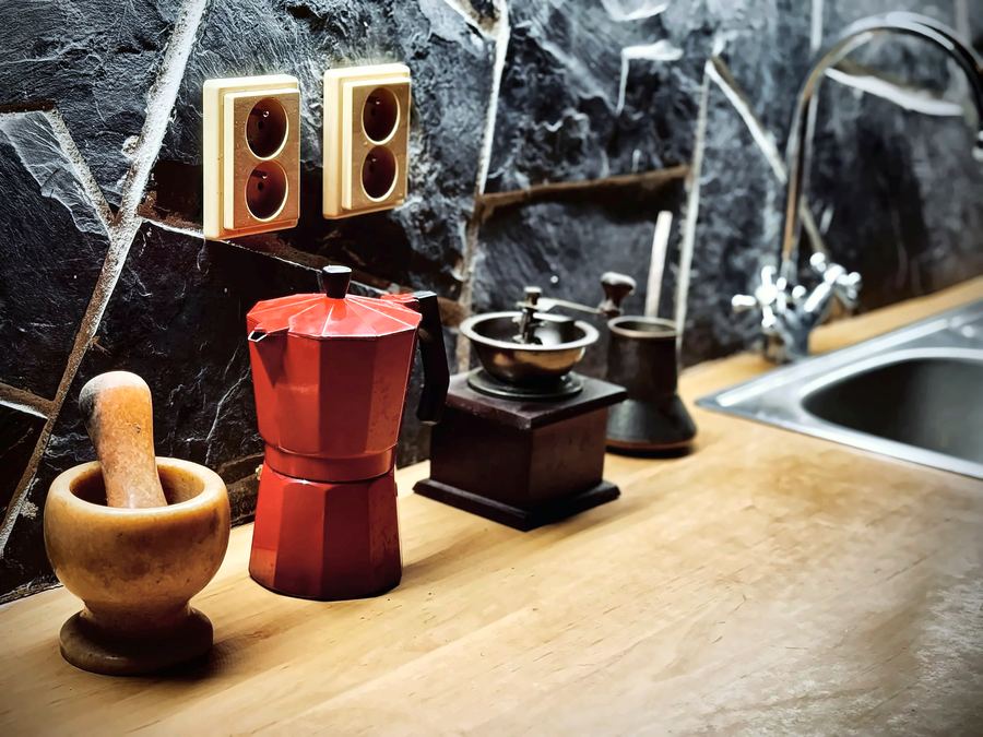 Červená moka konvice, ruční mlýnek na kávu a hmoždíř na kuchyňské desce