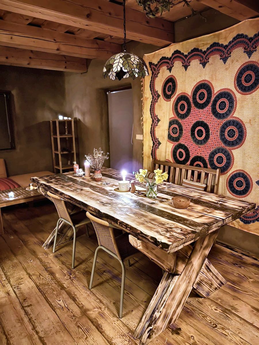 Dlouhý dřevěný stůl se svíčkami, na stěně ornamentální textilie